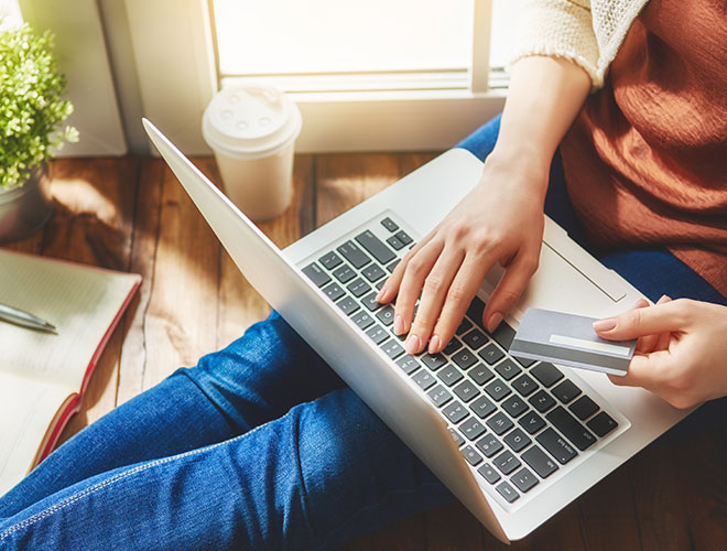 Frau sitzt am Laptop und hält eine Kreditkarte in der Hand