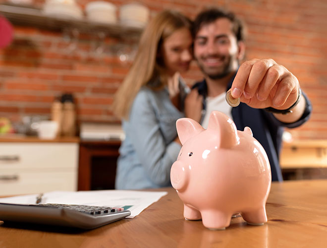 Sparen & Anlegen Junges Paar wirft Münzen in ein Sparschwein